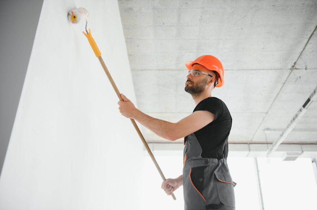 Building contractor painting grey wall with roller brush